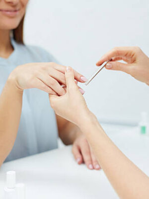 Young female showing her fingernails to manicurist polishing them