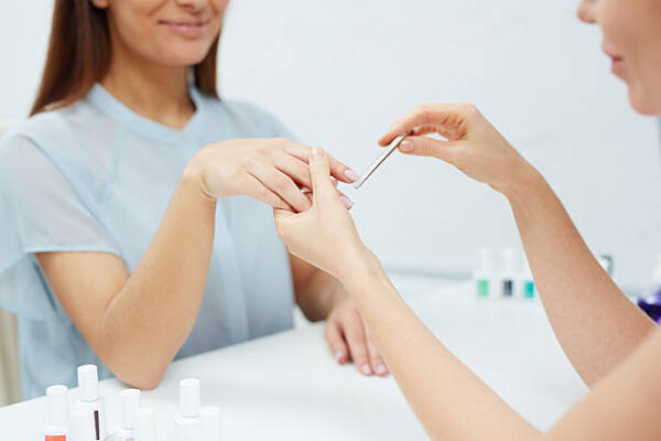Young female showing her fingernails to manicurist polishing them